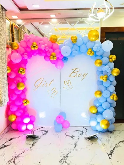 A "Girl or Boy" gender reveal backdrop with two arched panels. The setup is decorated with pink and blue balloon arches accented with gold balloons.