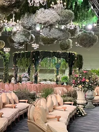 A wide view of the Italian garden reception, showcasing the circular seating arrangement, the floating floral clouds on the ceiling, and the central mandap, all unified by a palette of green and pastel florals.
