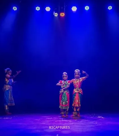 A group of dancers arranged in a creative formation at the 'SADHANA Dance Festival', with two dancers in the center and others surrounding them.
