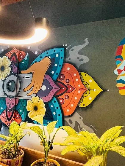 A wide shot of the completed mural at Photo Paparazzo, a photography studio in Champa Gali. The artwork spans the wall, creating a stunning backdrop that combines abstract portraits with a central camera motif.
