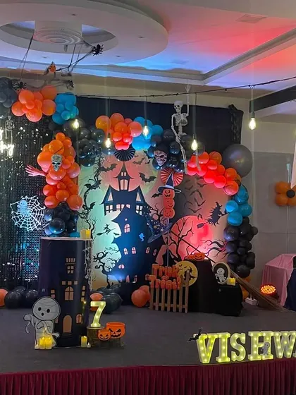 A spooky and fun Halloween themed birthday party. The large-scale decoration includes a haunted house backdrop, spider webs, ghosts, and a balloon arrangement in orange, black, and blue.