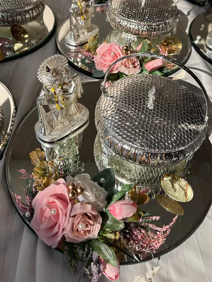 This silver-themed wedding favour is perfect for adding a touch of royalty. It features a mirrored tray with a silver-plated dry fruit box and a Ganesha idol, decorated with pink flowers for a soft, elegant look.