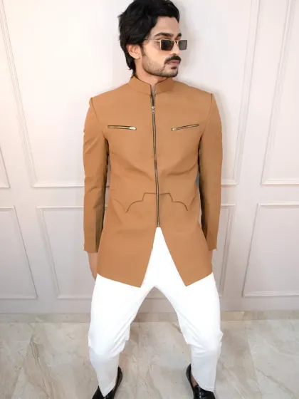 A modern tan bandhgala jacket with a full front zipper and functional zip pockets. Paired with white trousers, this creates a sharp, contemporary look for any celebration.