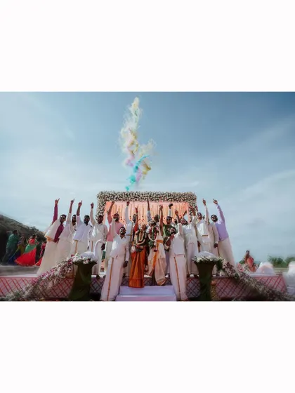An epic group photo of the wedding party celebrating with colored smoke against a bright blue sky.