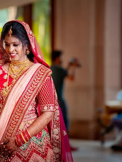 An elegant bride in her red and pink lehenga, captured in a moment of quiet grace at her wedding venue.