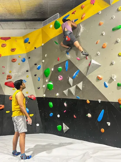 A climber works on a route while their partner spots them from below. This image captures the collaborative and supportive nature of our climbing community. We're all here to help each other succeed.