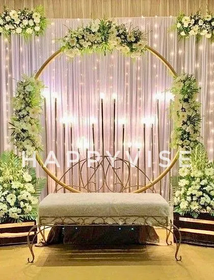 A beautiful stage setup featuring a golden ring arch adorned with white flowers and fairy lights. The wooden crates add a rustic yet elegant touch to the overall design.