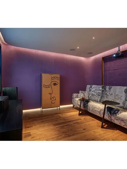 The home theatre is designed for a complete cinematic experience. We used a deep purple fabric on the walls for acoustics and ambiance, complemented by a custom-printed sofa and soft, indirect lighting.