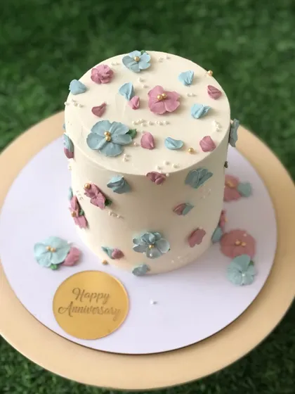 A delicate anniversary cake with scattered pastel blue and pink buttercream flowers.