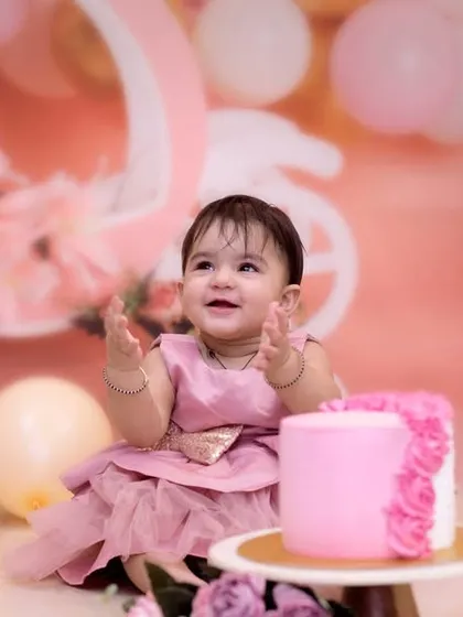 The moment of anticipation right before the cake smash begins. This little girl is all smiles, surrounded by a beautiful pink and gold setup for her first birthday.