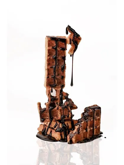 A creative and abstract food concept, showing a tower of waffles drizzled with chocolate sauce. This high-key shot isolates the subject, focusing on the unique form and texture for a memorable ad visual.