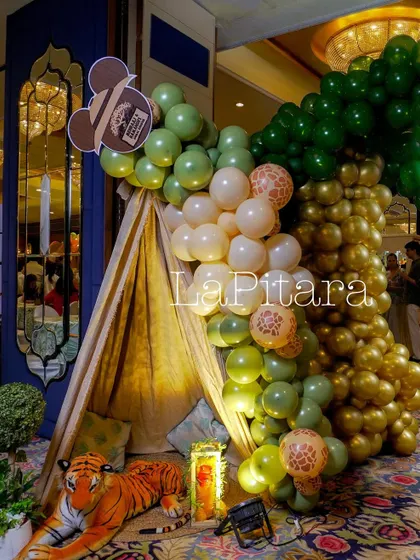 A cozy jungle-themed nook featuring a teepee, a plush tiger, and a cascading balloon garland in shades of green, gold, and animal print.