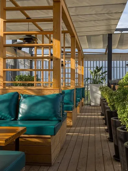 The rooftop terrace seating, with its wooden pergola and lush planters, offers a breezy and relaxing atmosphere. The design is meant to feel like an escape, high above the city streets.