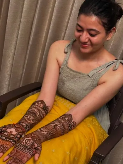 A happy client admiring her full-arm mehndi, which features the couple's initials 'DP' on the palm.