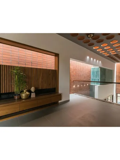 An upper-level corridor in 'An Earthy Affair' overlooks the central living space. We used a combination of brick jaalis and wooden louvers to create privacy while allowing light and air to flow freely through the home.