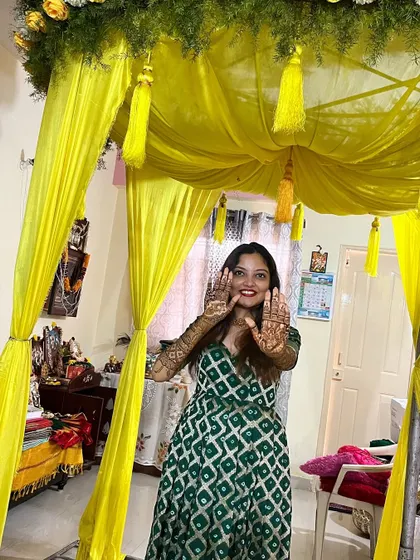 A happy client showing off her beautiful mehndi during her home ceremony. The festive yellow decor perfectly complements the traditional art on her hands.