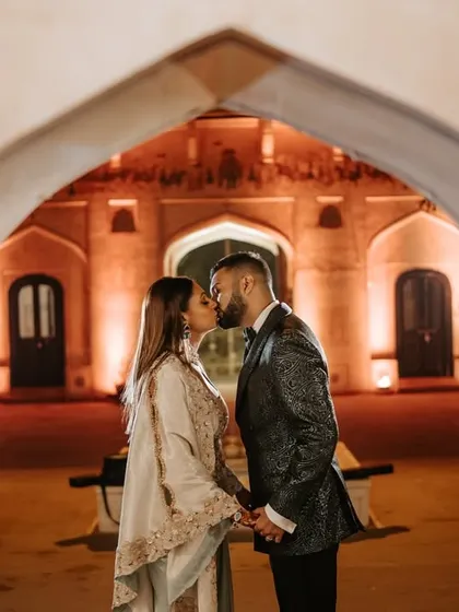A romantic kiss under an archway at their palace reception. The warm lighting and historic setting create a fairytale-like moment.