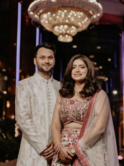 A classic portrait of the couple under a grand chandelier at their roka ceremony. Their elegant outfits and the luxurious setting create a timeless and sophisticated image.