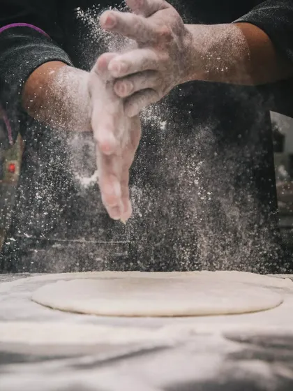 A chef dusts flour over fresh dough, preparing for a live pizza station.