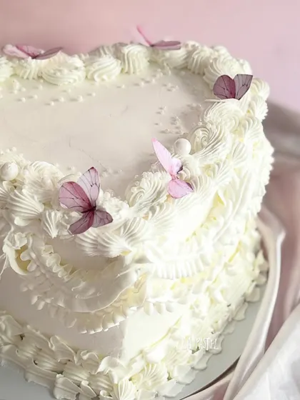 A beautiful heart-shaped cake with white piped frosting and delicate pink butterflies. This one was a strawberry Baileys cream flavor!