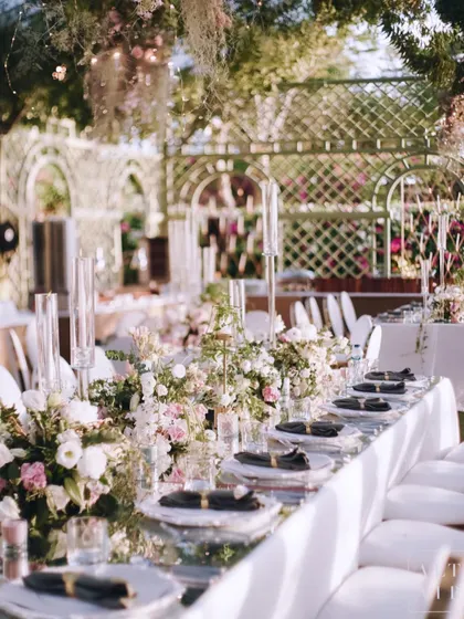 A long dining table at the 'Romantic Garden' reception, set against a backdrop of white trellis arches. The design was a celebration of love and romance in a beautiful natural setting.