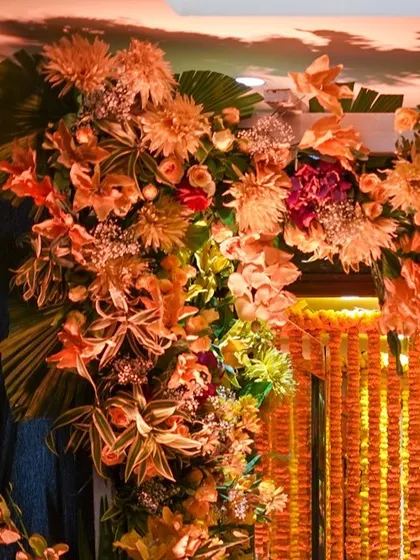 A lush floral arrangement framing a doorway, with a curtain of marigolds in the background. The mix of different flowers and foliage creates a rich and abundant look.