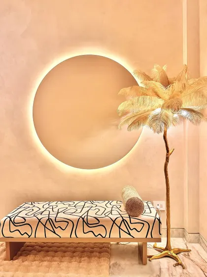 A quiet corner in the bedroom, featuring a custom bench with abstract fabric and a sculptural floor lamp with feather-like details. The circular backlit wall feature creates a soft, halo-like glow, adding to the room's serene and artistic ambiance.