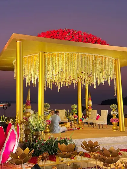 The golden structure of the 'Kamal Palace' mandap, adorned with a roof of red roses and tuberose garlands, set against the purple Goan twilight.