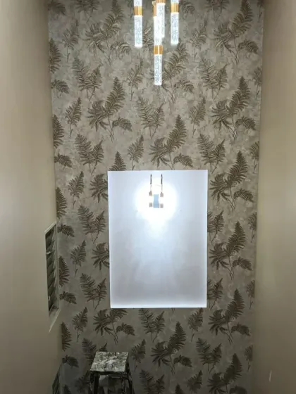A fern leaf pattern wallpaper installed on a double-height wall. The metallic gold accents in the design catch the light beautifully.