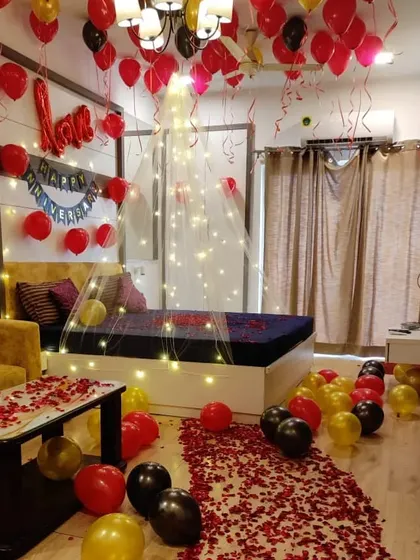 A complete room makeover for a birthday, featuring a romantic bed canopy, a rose petal walkway, and balloons in red, black, and gold.