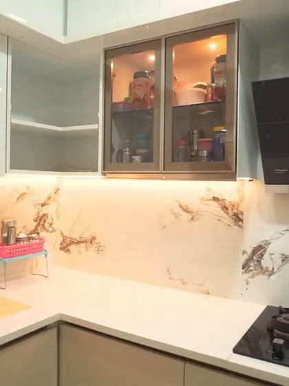 A close-up of the cooking area, showing the hob and chimney against the marble-effect backsplash. The combination of white, gold, and marble creates a luxurious and timeless feel.
