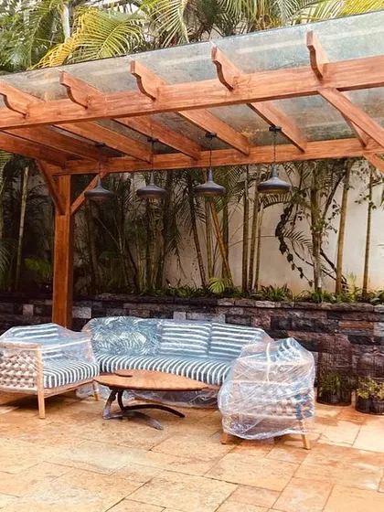 A glass-roofed pergola provides a sheltered outdoor seating area. We designed this space with a stone feature wall and surrounding bamboo to create a private, resort-like feel within the client's garden.