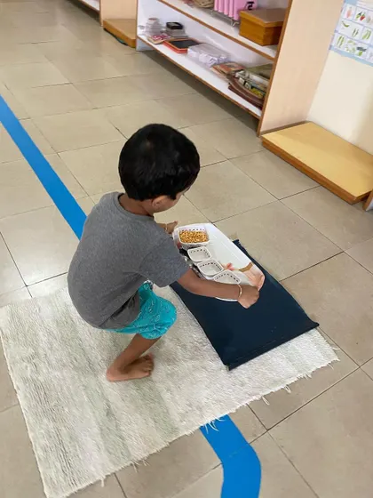 A child carefully places his snack tray on his work mat. This sequence of actions teaches order, planning, and respect for one's personal workspace.