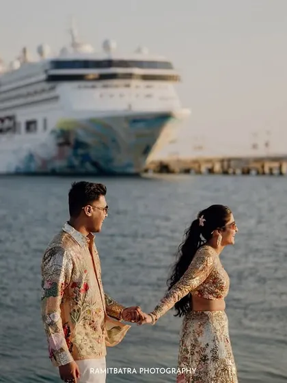 The couple holds hands on the pier, with their magnificent cruise ship waiting in the background, ready to set sail.
