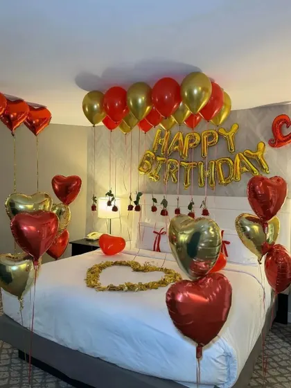 A full view of the red and gold romantic birthday setup, with 'Happy Birthday' foil letters above the bed.