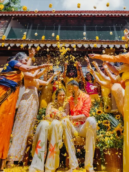 A shower of yellow flower petals rains down on the couple, creating a picture-perfect moment of celebration at their Haldi.