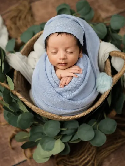 A beautiful overhead view of a baby sleeping peacefully in a basket. The ring of eucalyptus leaves creates a natural and organic frame.