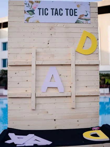 A giant, rustic Tic-Tac-Toe game board, personalized with the couple's initials, adding a fun and interactive element to their pre-wedding carnival.