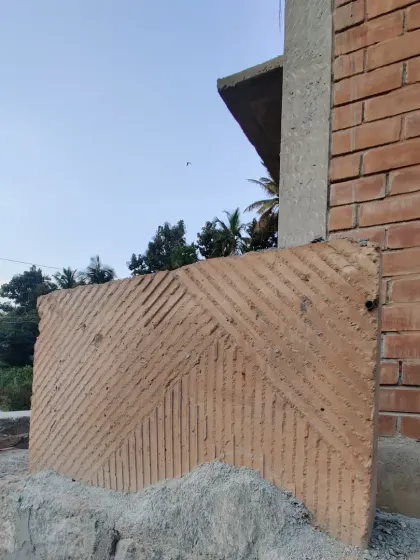A test panel of poured earth with a geometric pattern, resting against a brick wall on site.