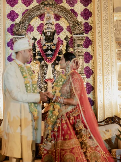 A close up of the couple during the ceremony, with the deity of Tirupati Balaji, framed by a wall of flowers, watching over their union. This detail highlights the spiritual core of the design.