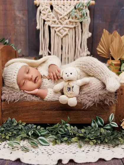 A full view of a sleeping newborn in a rustic wooden bed, surrounded by greenery and boho-chic decor.