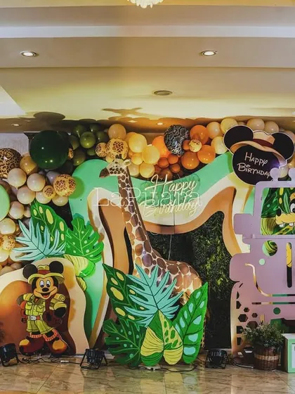 A full view of the colorful jungle safari photo wall, featuring a giraffe, a jeep, and large letter blocks spelling 'ONE' and 'TWO'.