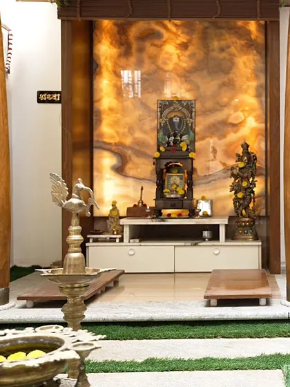 A direct view of the pooja room, highlighting the beautiful patterns in the backlit onyx panel. The space is set within an artificial grass patch with stone steps, enhancing the feeling of a natural, sacred grove.