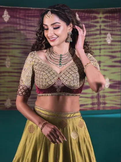 A smiling portrait of the model in the olive green lehenga, showcasing her elegant jewelry and the flattering fit of the custom-designed blouse.