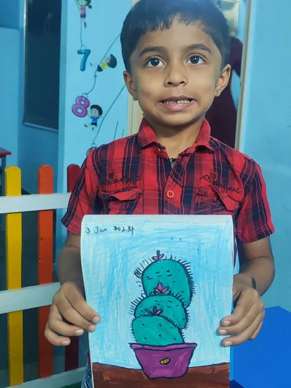 A proud student holding his colorful drawing of a cactus plant in a purple pot.