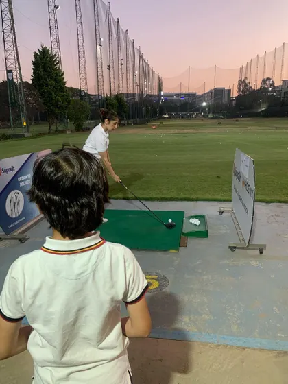 A young golfer watches intently as an adult practices her putting. It's great to see the next generation learning from others at the course.
