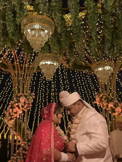 A sacred moment during the wedding ceremony, with the couple framed by the golden mandap structure, hanging chandeliers, and a sky of lights.