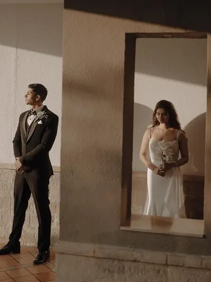 A beautiful, artistic shot capturing the first look between the bride and groom, with the groom waiting as the bride is framed in a window.