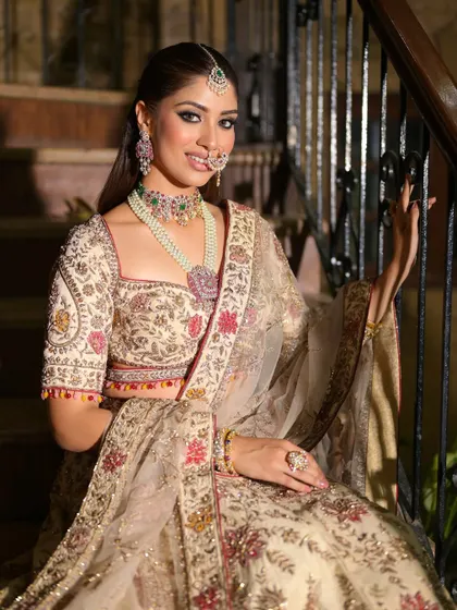 A look full of regal elegance. This bride is seated on a staircase, her ivory and floral lehenga creating a beautiful picture. The makeup is soft yet defined, perfect for her reception.