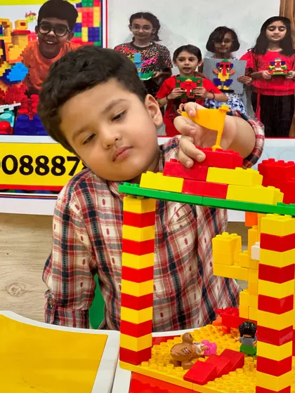 A young builder concentrates on adding the final touches to his tall LEGO tower, learning about structural stability.